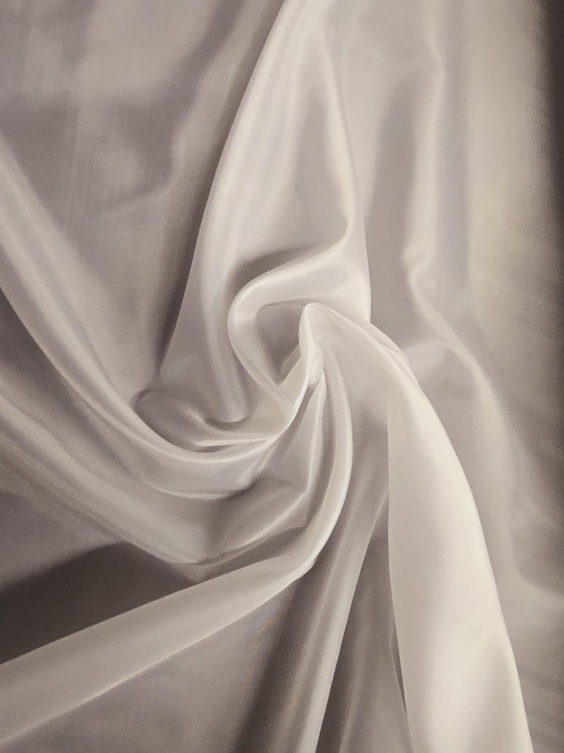 Puede incluir: Tela blanca transparente con una textura suave y fluida. La tela est&aacute; drapeada y doblada, creando un aspecto liso y elegante.