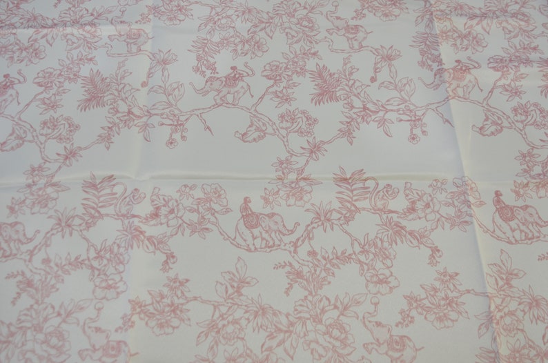 May include: White fabric with a pink floral pattern featuring elephants, monkeys, and peacocks. The pattern is repeated throughout the fabric.
