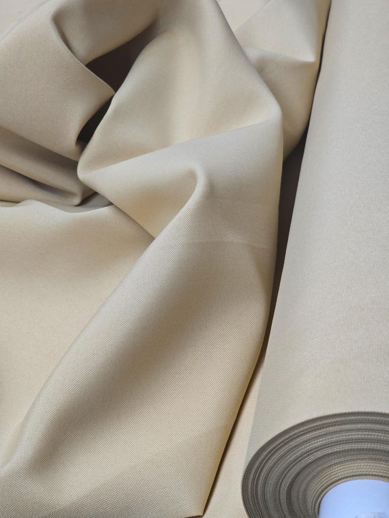 Puede incluir: Un rollo de tela beige con una textura lisa y uniforme. La tela est&aacute; doblada y enrollada, mostrando el ancho y la forma en que se drape.