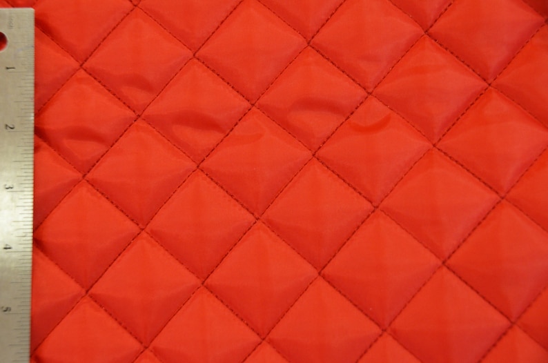 May include: Red quilted fabric with a diamond pattern. The fabric is smooth and has a slight sheen.