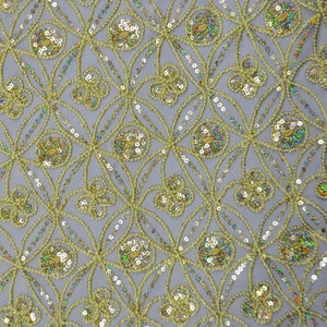 May include: A close-up of a light blue fabric with a repeating pattern of gold sequins. The sequins are arranged in a geometric design, creating a shimmering effect.