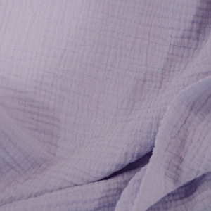 May include: A close-up of a soft, light purple fabric with a crinkled texture. The fabric is folded and draped, showing its texture and drape.