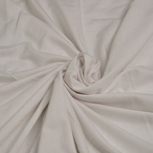 May include: A close-up of a white fabric with a soft, smooth texture. The fabric is folded and draped in a way that creates a swirling, organic pattern.