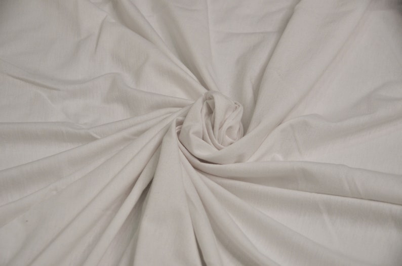 May include: A close-up of a white fabric with a soft, smooth texture. The fabric is folded and draped in a way that creates a swirling, organic pattern.