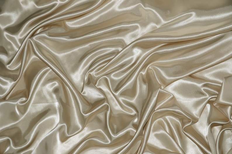 May include: A smooth, silky fabric in a light beige color. The fabric is draped and folded, creating soft, flowing lines and curves.