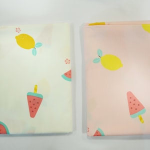 May include: Two fabric squares with a summer fruit theme. One square is white with a lemon and watermelon popsicle design. The other square is pink with a lemon and watermelon popsicle design.