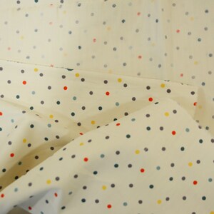 May include: Cream-colored fabric with a repeating pattern of small, colorful polka dots. The dots are in shades of red, yellow, blue, and gray.