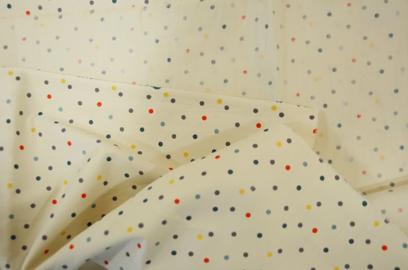 May include: Cream-colored fabric with a repeating pattern of small, colorful polka dots. The dots are in shades of red, yellow, blue, and gray.