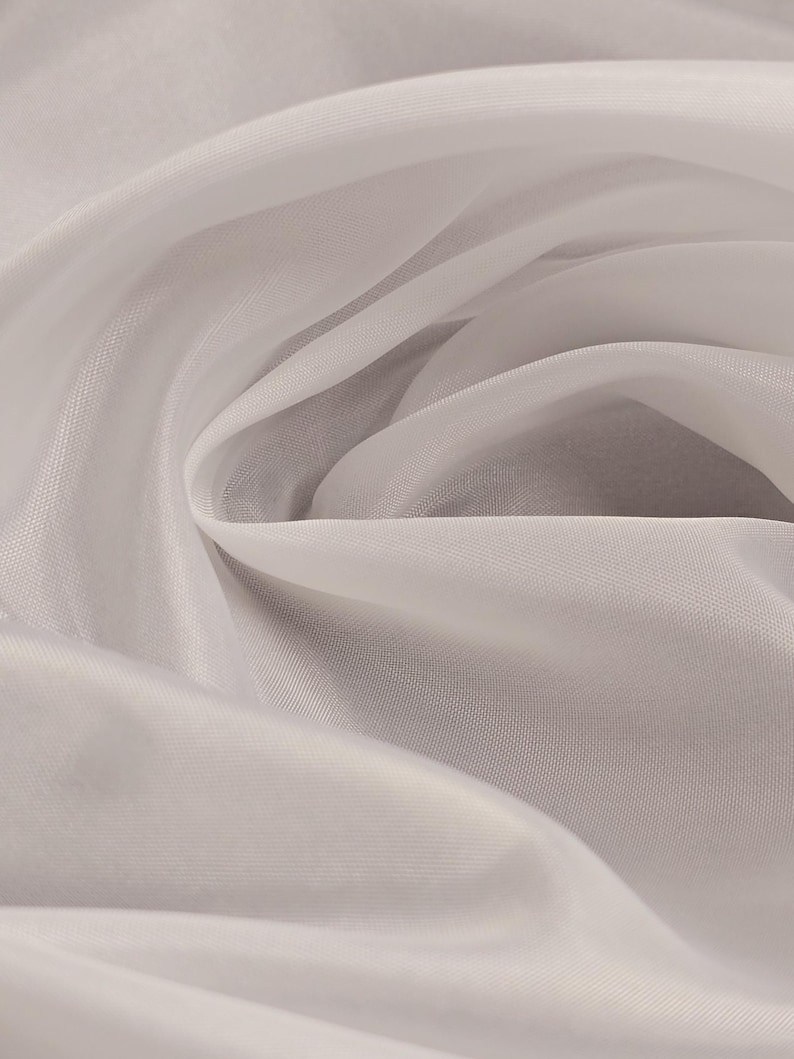 Puede incluir: Tela blanca transparente con una textura suave y fluida. La tela est&aacute; drapeada y doblada, creando un aspecto liso y elegante.