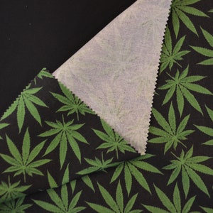 May include: Black fabric with a green marijuana leaf pattern. The fabric is folded over to show the white underside.