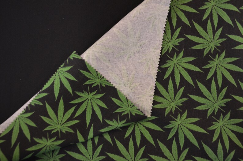 May include: Black fabric with a green marijuana leaf pattern. The fabric is folded over to show the white underside.