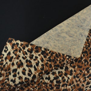 Op de afbeelding: Close-up van een beige stof met een bruine en zwarte luipaardprint. De stof is dubbelgevouwen, waardoor een beige en blauwe marmerprint aan de onderkant zichtbaar is.
