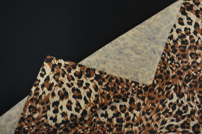 Op de afbeelding: Close-up van een beige stof met een bruine en zwarte luipaardprint. De stof is dubbelgevouwen, waardoor een beige en blauwe marmerprint aan de onderkant zichtbaar is.