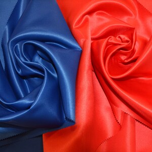 Puede incluir: Primer plano de dos muestras de tela, una de color azul oscuro y la otra de color rojo brillante. Ambas telas son lisas y tienen un acabado satinado.