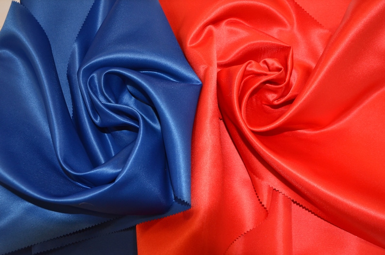 Puede incluir: Primer plano de dos muestras de tela, una de color azul oscuro y la otra de color rojo brillante. Ambas telas son lisas y tienen un acabado satinado.