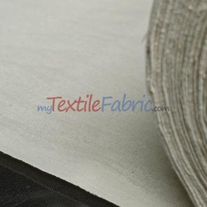 Może przedstawiać: Zbliżenie na rolkę beżowej tkaniny o widocznej fakturze. Tekst "myTextileFabric.com" jest wydrukowany w kolorze niebieskim i czerwonym. Czarna krawędź tkaniny jest widoczna na dole. Tkanina jest trudnopalna.
