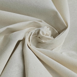 May include: Close-up of a natural, off-white fabric with a smooth, woven texture. The fabric is folded and draped, showcasing its soft and pliable nature.