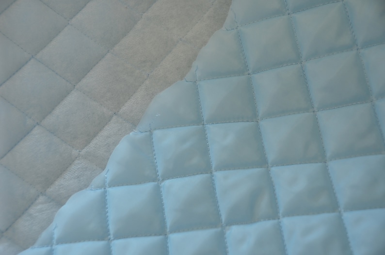 May include: A close-up of a light blue quilted fabric with a diamond pattern. The fabric is soft and smooth, and the quilting is evenly spaced.