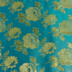 May include: Teal fabric with a gold floral pattern. The fabric has a brocade texture and is woven with a repeating pattern of flowers and leaves.