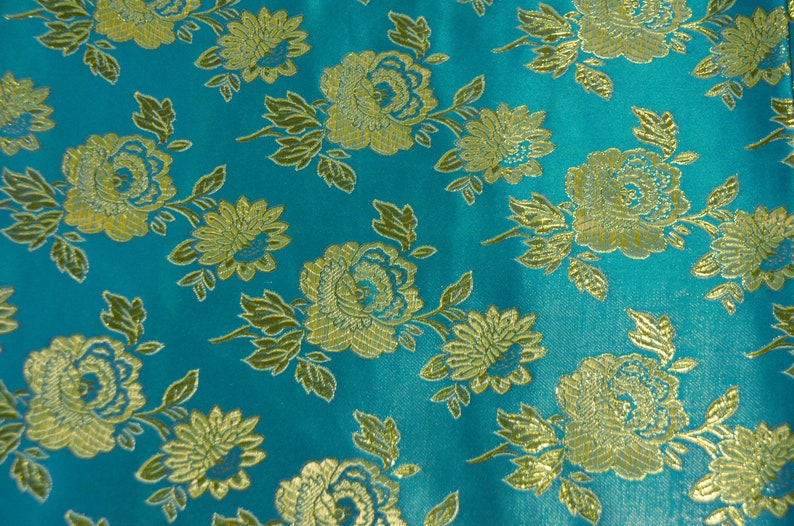 May include: Teal fabric with a gold floral pattern. The fabric has a brocade texture and is woven with a repeating pattern of flowers and leaves.