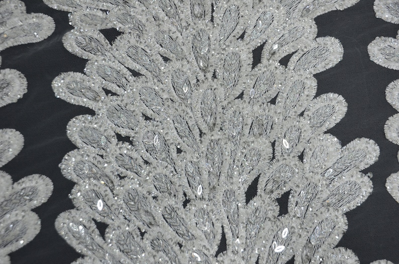Puede incluir: Tela blanca con cuentas con un delicado patr&oacute;n de plumas. La tela es transparente y tiene un brillo sutil.