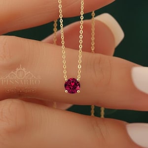 May include: A delicate gold necklace featuring a round, vibrant red gemstone pendant. The chain is thin and elegant, showcasing the gemstone's rich color. The necklace is a classic piece of jewelry.