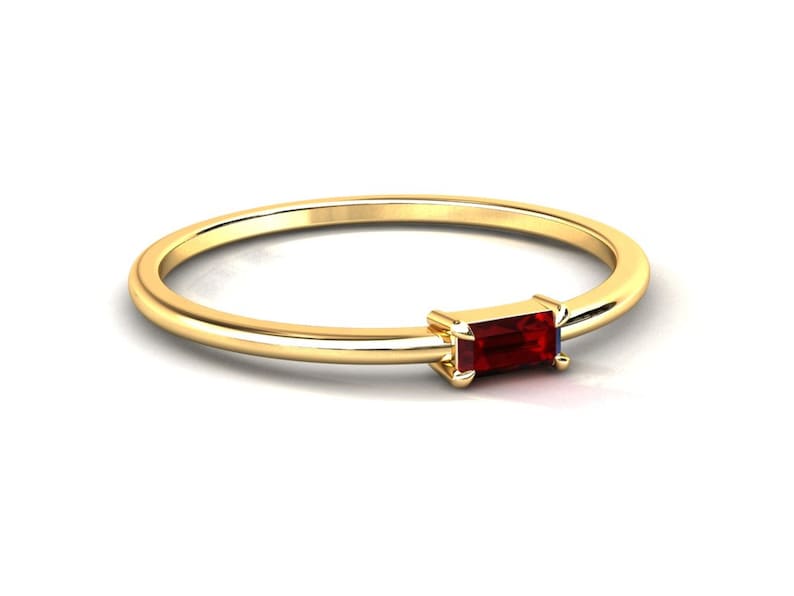 May include: A simple gold band ring with a small, rectangular, red gemstone set in the center.