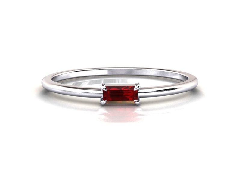 May include: A simple silver band ring with a small, rectangular red gemstone set in the center.