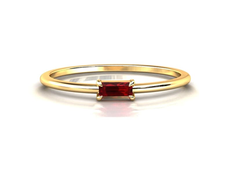May include: A delicate gold band ring with a small, rectangular red gemstone set in the center.