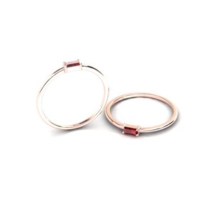 May include: Two delicate gold rings with a single red gemstone set in each. The rings are simple and elegant, perfect for everyday wear.