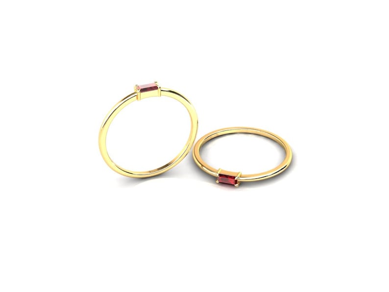May include: Two gold rings with a single red gemstone set in each. The rings are simple and delicate.