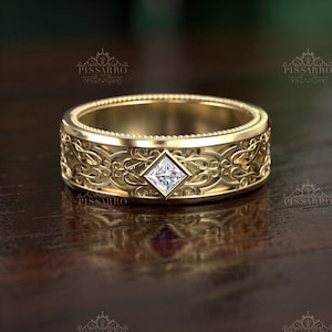 May include: A gold-colored ring with an intricate floral design and a square, clear gemstone at the center. The ring has a wide band with detailed patterns and a polished finish, suitable for a wedding or engagement.