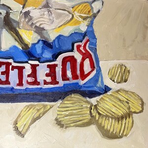 May include: A blue bag of potato chips with the word "DORITOS" printed in red and white. The bag is open and there are several potato chips scattered on a white surface.