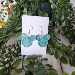 May include: A pair of turquoise blue sparkly Mickey Mouse earrings. The earrings are on a white card.