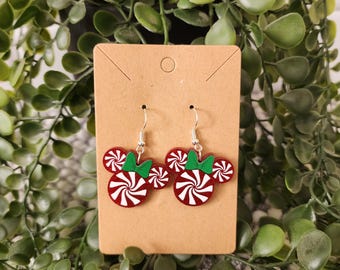 May include: Red and white candy cane earrings with green bows, shaped like Mickey Mouse ears. The earrings are on a brown card.
