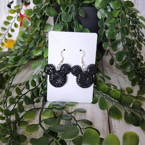 May include: Black sparkly Mickey Mouse earrings on a white display card. The earrings are silver and have a black, sparkly Mickey Mouse head charm.