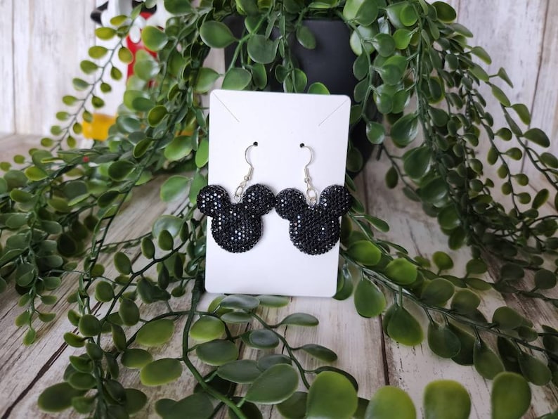 May include: Black sparkly Mickey Mouse earrings on a white display card. The earrings are silver and have a black, sparkly Mickey Mouse head charm.