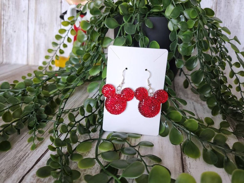 May include: Red rhinestone Mickey Mouse earrings with silver hooks. The earrings are displayed on a white card.