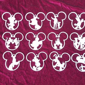 May include: Twelve white, cutout ornaments shaped like Mickey Mouse's head. Each ornament features a different silhouette of a Disney character, including Mickey Mouse, Minnie Mouse, Donald Duck, Goofy, and others.