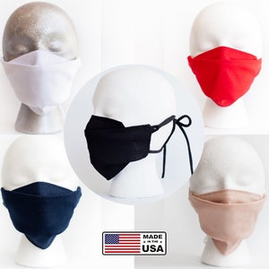 May include: Five face masks on mannequin heads, each mask is a different color: white, red, black, navy blue, and beige. The masks are made in the USA.