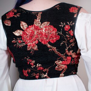 May include: A black velvet vest with a red and gold floral pattern. The vest has a scoop neck and a sleeveless design.