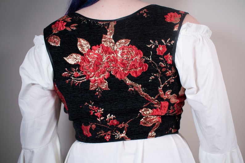 May include: A black velvet vest with a red and gold floral pattern. The vest has a scoop neck and a sleeveless design.