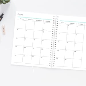 Pode incluir: Um planejador espiralado aberto com um calend&aacute;rio de janeiro. A grade do calend&aacute;rio &eacute; preta sobre branco, com os dias da semana em espanhol. Uma caneta e pequenos clipes de madeira s&atilde;o vis&iacute;veis na superf&iacute;cie branca. A palavra 'Enero' est&aacute; no topo.