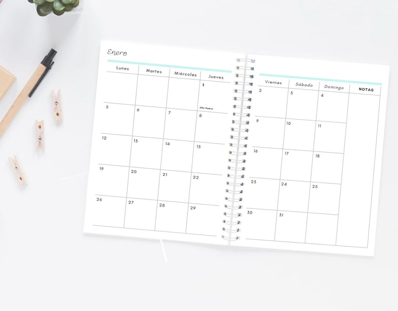Pode incluir: Um planejador espiralado aberto com um calend&aacute;rio de janeiro. A grade do calend&aacute;rio &eacute; preta sobre branco, com os dias da semana em espanhol. Uma caneta e pequenos clipes de madeira s&atilde;o vis&iacute;veis na superf&iacute;cie branca. A palavra 'Enero' est&aacute; no topo.