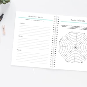 Pode incluir: Caderno aberto com espiral, com p&aacute;ginas pautadas e um diagrama da roda da vida. A p&aacute;gina esquerda tem se&ccedil;&otilde;es para afirma&ccedil;&otilde;es da manh&atilde;, da tarde e da noite. A p&aacute;gina direita apresenta um diagrama circular.