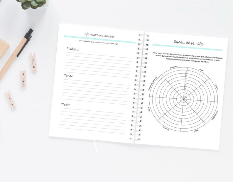Pode incluir: Caderno aberto com espiral, com p&aacute;ginas pautadas e um diagrama da roda da vida. A p&aacute;gina esquerda tem se&ccedil;&otilde;es para afirma&ccedil;&otilde;es da manh&atilde;, da tarde e da noite. A p&aacute;gina direita apresenta um diagrama circular.