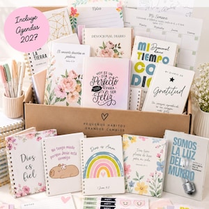 Pode incluir: Uma coleção de artigos de papelaria com temática cristã, incluindo diários espirais, agendas e blocos de notas com desenhos florais e de arco-íris. Os itens apresentam textos em espanhol como "Hoy es un día perfecto para ser feliz" e "Dios es fiel" dentro de uma caixa de papelão.