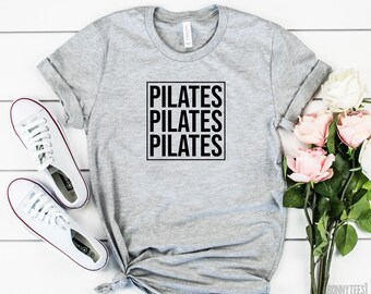 May include: Gray t-shirt with the text "PILATES" repeated three times in a black box.