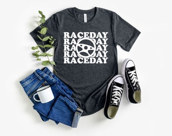 Könnte beinhalten: Ein dunkelgraues T-Shirt mit einer weißen Grafik eines Lenkrads und dem Text "RACEDAY", der viermal wiederholt wird.