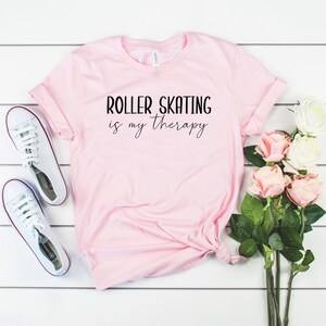 May include: Pink t-shirt with the text "Roller Skating is my therapy" in black lettering.